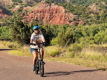 Middle-aged woman riding Qualisports' Dolphin electric bike passing through mountain road