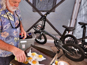 Middle-aged man with Dolphin electric bike taking a break at the campsite, cooking sunny-side-up eggs